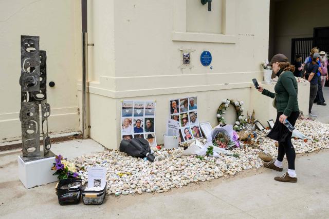 A woman takes pictures of flowers and photos seen in memory of the victims of December 14 Bondi Beach shooting at the Bondi Pavilion in Sydney on January 22, 2026, as part of the national day of mourning. Australians will light candles and fall silent on January 22, on a national day of mourning for the 15 people killed by gunmen who opened fire on a Jewish festival at Bondi Beach. (Photo by Steven Markham / AFP)