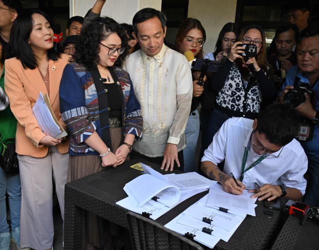 A lawyer (seated R) signs documents as he verifies the impeachment complaint against Philippine President Ferdinand Marcos prior to submitting them to the of the Secretary General in the House of Representatives in Quezon City, suburban Manila on January 22, 2026, alonside legislators of the progressive group Sara Elago (L standing), Louise Co (C) and Antonio Tinio (R). (Photo by Ted ALJIBE / AFP)
