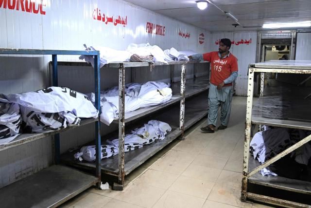 A volunteer arranges bodies of victims inside a hospital morgue in Karachi on January 21, 2026 following a massive fire at a shopping mall. Pakistani rescuers scoured the charred remains of a Karachi mall on January 21 for dozens missing after a huge blaze destroyed the complex, while relatives gave DNA samples to aid the search. (Photo by Rizwan TABASSUM / AFP)