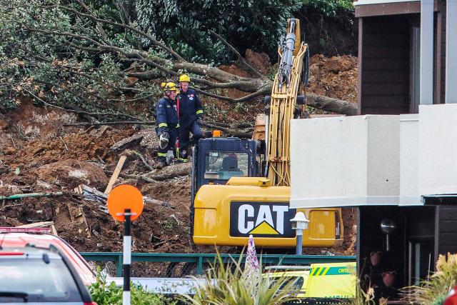 Police and officials stand following a landslide while a search is underway by local emergency services for missing people at Mount Maunganui in Tauranga on January 22, 2026. A landslide smashed into a campsite in rain-swept northern New Zealand leaving multiple people missing, police and rescuers said. (Photo by DJ MILLS / AFP)