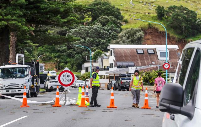Emergency workers close a road following a landslide while a search is underway by local emergency services for missing people at Mount Maunganui in Tauranga on January 22, 2026. A landslide smashed into a campsite in rain-swept northern New Zealand leaving multiple people missing, police and rescuers said. (Photo by DJ MILLS / AFP)