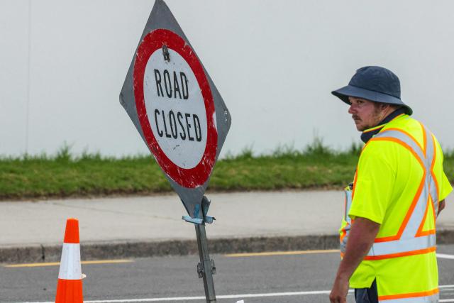 Emergency workers close a road following a landslide while a search is underway by local emergency services for missing people at Mount Maunganui in Tauranga on January 22, 2026. A landslide smashed into a campsite in rain-swept northern New Zealand leaving multiple people missing, police and rescuers said. (Photo by DJ MILLS / AFP)