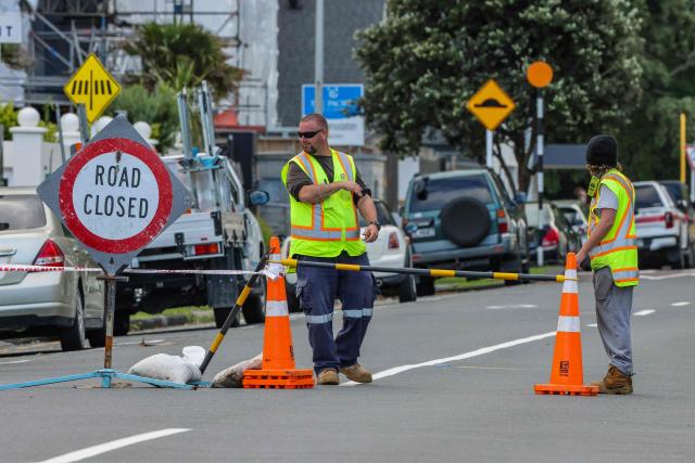 Emergency workers close a road following a landslide while a search is underway by local emergency services for missing people at Mount Maunganui in Tauranga on January 22, 2026. A landslide smashed into a campsite in rain-swept northern New Zealand leaving multiple people missing, police and rescuers said. (Photo by DJ MILLS / AFP)