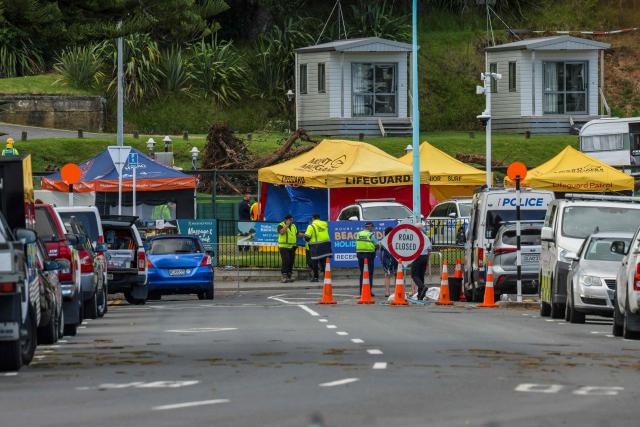 Emergency workers close a road following a landslide while a search is underway by local emergency services for missing people at Mount Maunganui in Tauranga on January 22, 2026. A landslide smashed into a campsite in rain-swept northern New Zealand leaving multiple people missing, police and rescuers said. (Photo by DJ MILLS / AFP)
