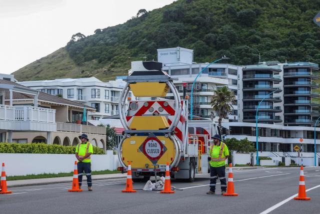 Emergency workers close a road following a landslide while a search is underway by local emergency services for missing people at Mount Maunganui in Tauranga on January 22, 2026. A landslide smashed into a campsite in rain-swept northern New Zealand leaving multiple people missing, police and rescuers said. (Photo by DJ MILLS / AFP)