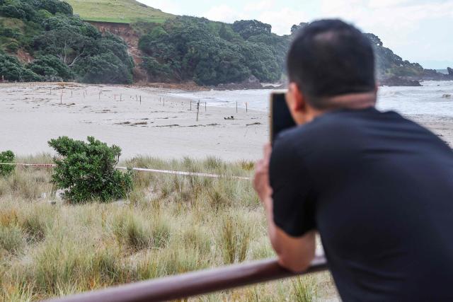 A man takes photos of a landslide while a search is underway by local emergency services for missing people at Mount Maunganui in Tauranga on January 22, 2026. A landslide smashed into a campsite in rain-swept northern New Zealand leaving multiple people missing, police and rescuers said. (Photo by DJ MILLS / AFP)