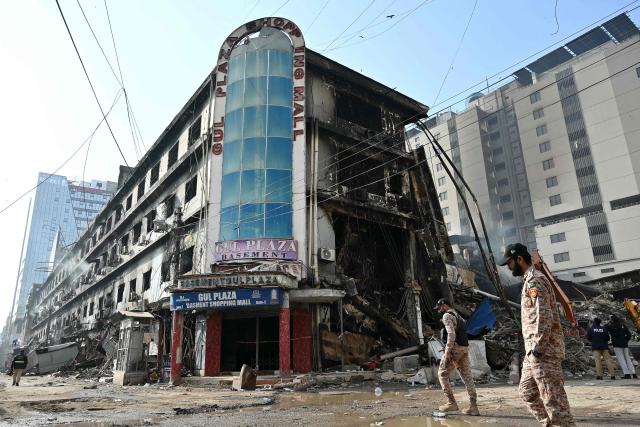 Pakistan's paramilitary personnel walk past charred remains of a shopping mall in Karachi on January 22, 2026, after a massive fire broke out on January 17. The death toll from a mall fire in Pakistan's biggest city rose to at least 55 people, a Karachi government official told AFP on January 22. (Photo by Asif HASSAN / AFP)