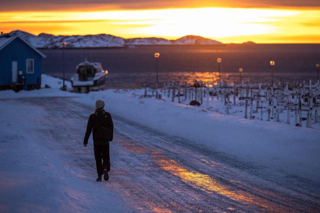 A person walks along an icy road reflecting the light of the setting sun in Nuuk, Greenland, on January 21, 2026. The US President will show off his new "Board of Peace" at Davos on January 22, 2026, burnishing his claim to be a peacemaker a day after backing off his own threats against Greenland. (Photo by Jonathan NACKSTRAND / AFP)