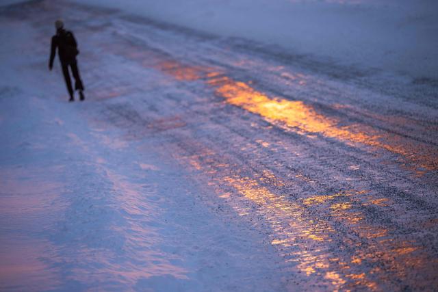A person walks along an icy road reflecting the light of the setting sun in Nuuk, Greenland, on January 21, 2026. The US President will show off his new "Board of Peace" at Davos on January 22, 2026, burnishing his claim to be a peacemaker a day after backing off his own threats against Greenland. (Photo by Jonathan NACKSTRAND / AFP)