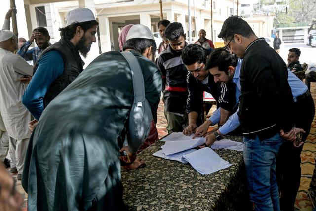People check names of missing relatives on a list after a massive fire broke out at a shopping mall in Karachi on January 22, 2026. The death toll from a mall fire in Pakistan's biggest city rose to at least 55 people, a Karachi government official told AFP on January 22. (Photo by Rizwan TABASSUM / AFP)