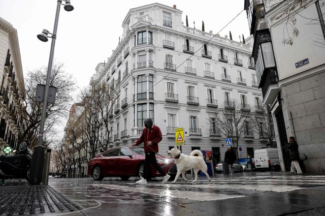 A man walks his dog in Jorge Juan street in Madrid on January 21, 2026. Madrid has emerged as a coveted global luxury housing destination as Latin American and US investors fuel a real estate boom, seduced by competitive prices and high living standards. (Photo by OSCAR DEL POZO / AFP)