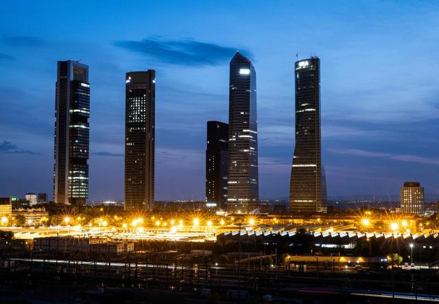 (FILES) General view of Madrid’s Cuatro Torres business district illuminated at dusk is pictured on August 13, 2025. Madrid has emerged as a coveted global luxury housing destination as Latin American and US investors fuel a real estate boom, seduced by competitive prices and high living standards. (Photo by OSCAR DEL POZO / AFP)
