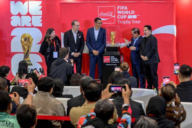 (L-R) President Director of Coca-Cola Indonesia Eva Lusiana, President of the Coca-Cola Company for ASEAN and South Pacific Selman Careaga, former Brazil player Gilberto Silva, Governor of Jakarta Pramono Anung, Minister of Youth and Sports Erick Thohir, and members of the Indonesian public look at the trophy during the original FIFA World Cup 2026 Trophy Tour in Jakarta on January 22, 2026. (Photo by BAY ISMOYO / AFP)