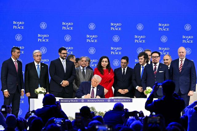 Paraguay's President Santiago Pena (L), Pakistan's Prime Minister Shehbaz Sharif (5L), Kosovo's President Vjosa Osmani (C-R), Morocco's Foreign Minister Nasser Bourita (6R), Argentina's President Javier Milei (5R), Armenia's Prime Minister Nikol Pashinyan (2R), Bulgaria's former Prime Minister Rosen Zhelyazkov (R), Turkey's Foreign Minister Hakan Fidan (4R) pose with US President Donald Trump signing a founding charter at the "Board of Peace" meeting during the World Economic Forum (WEF) annual meeting in Davos on January 22, 2026. US President Donald Trump will show off his new "Board of Peace" at Davos on January 22, 2026 burnishing his claim to be a peacemaker a day after backing off his own threats against Greenland. Originally meant to oversee the rebuilding of Gaza after the war between Hamas and Israel, the board's charter does not limit its role to the Strip, and has sparked concerns that Trump wants it to rival the United Nations. (Photo by Fabrice COFFRINI / AFP)