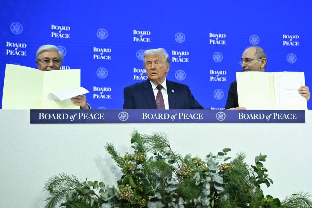Kazakh President Kassym-Jomart Tokayev (L) and Jordan's Foreign Minister Ayman Safadi (R) hold a signed founding charter as US President Donald Trump reacts at the "Board of Peace" meeting during the World Economic Forum (WEF) annual meeting in Davos on January 22, 2026. US President Donald Trump will show off his new "Board of Peace" at Davos on January 22, 2026 burnishing his claim to be a peacemaker a day after backing off his own threats against Greenland. Originally meant to oversee the rebuilding of Gaza after the war between Hamas and Israel, the board's charter does not limit its role to the Strip, and has sparked concerns that Trump wants it to rival the United Nations. (Photo by Mandel NGAN / AFP)