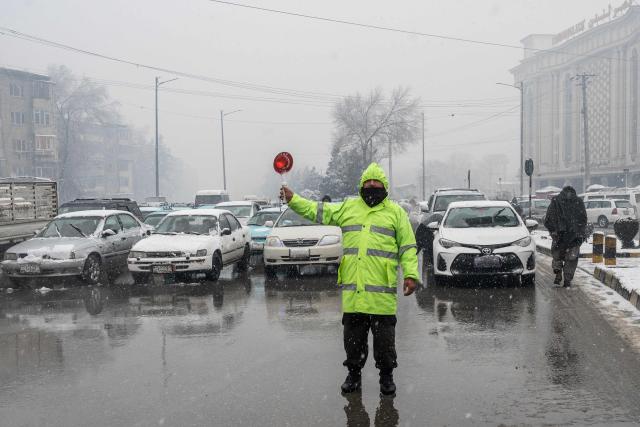 An Afghan traffic policeman controls traffic along a road during snowfall in Kabul on January 22, 2026. Severe storms and a rain-triggered landslide have killed at least nine children across southern and eastern Afghanistan, officials said, with residents facing further risks as heavy snow hits the country. (Photo by Wakil KOHSAR / AFP)