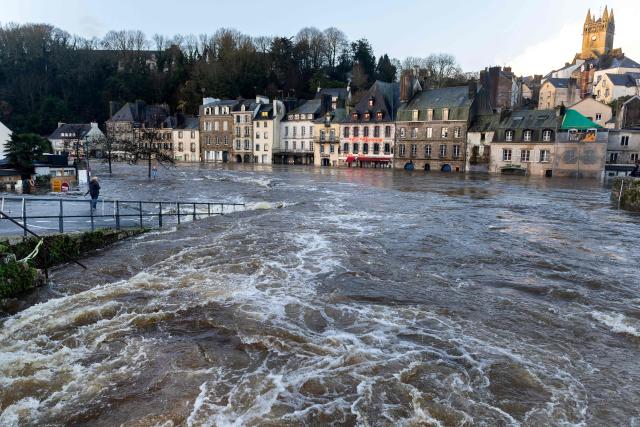 A man holding an umbrella looks at a flooded street in Quimperle, western France on January 22, 2026. Finistиre and Morbihan departments of western France are on orange alert on January 21, 2026, for “rain and flooding”. (Photo by Fred TANNEAU / AFP)