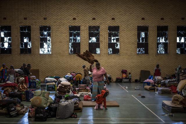 A woman, displaced from the informal settlement of Sporong by the ongoing unrest between the community and  a group of artisanal miners commonly referred to as "zama zamas", shakes her blanket at the Randgate Community Hall in Randfontein, on January 22, 2026 where the displaced took refuge. Residents and local officials blame artisanal miners, long associated with sudden eruptions of violence, running gun battles and the shadowy networks that sustain South Africa's illicit gold trade. 
Known locally as "zama zamas" -- "those who try" in the Zulu language -- they have become an entrenched presence in the shantytowns that ring Johannesburg and its satellite settlements along the gold reef. (Photo by MARCO LONGARI / AFP)