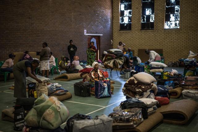 An elderly woman, displaced from the informal settlement of Sporong by the ongoing unrest between the community and  a group of artisanal miners commonly referred to as "zama zamas", keeps her belongings close to her at the Randgate Community Hall in Randfontein, on January 22, 2026 where the displaced took refuge. Residents and local officials blame artisanal miners, long associated with sudden eruptions of violence, running gun battles and the shadowy networks that sustain South Africa's illicit gold trade. 
Known locally as "zama zamas" -- "those who try" in the Zulu language -- they have become an entrenched presence in the shantytowns that ring Johannesburg and its satellite settlements along the gold reef. (Photo by MARCO LONGARI / AFP)
