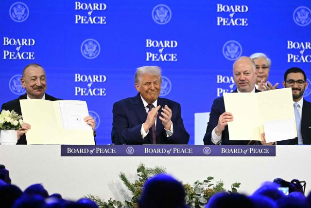 Azerbaijan's President Ilham Aliyev (L) and Bulgaria's former Prime Minister Rosen Zhelyazkov (R) hold a signed founding charter as US President Donald Trump applauds at the "Board of Peace" meeting during the World Economic Forum (WEF) annual meeting in Davos on January 22, 2026. US President Donald Trump will show off his new "Board of Peace" at Davos on January 22, 2026 burnishing his claim to be a peacemaker a day after backing off his own threats against Greenland. Originally meant to oversee the rebuilding of Gaza after the war between Hamas and Israel, the board's charter does not limit its role to the Strip, and has sparked concerns that Trump wants it to rival the United Nations. (Photo by Fabrice COFFRINI / AFP)