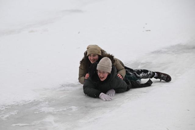 Schoolchildren sled down the slope during an air raid alert in a park in Kyiv on January 22, 2026, amid the Russian invasion of Ukraine. Schools in Ukraine's capital remain closed until February due to Russian strikes battered the energy sector amid below-freezing temperatures. (Photo by Sergei GAPON / AFP)