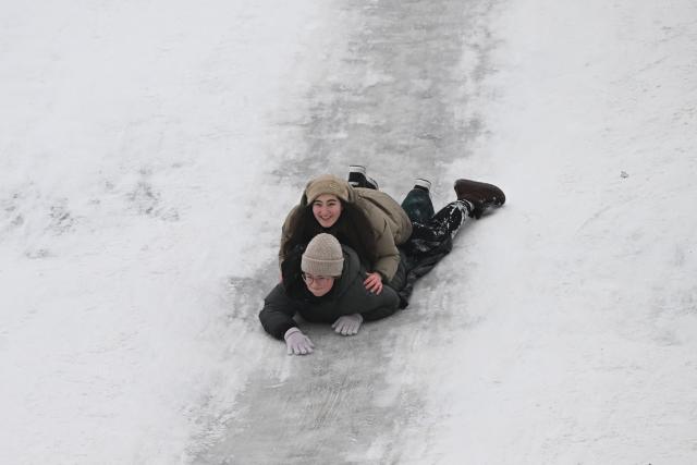 Schoolchildren sled down the slope during an air raid alert in a park in Kyiv on January 22, 2026, amid the Russian invasion of Ukraine. Schools in Ukraine's capital remain closed until February due to Russian strikes battered the energy sector amid below-freezing temperatures. (Photo by Sergei GAPON / AFP)