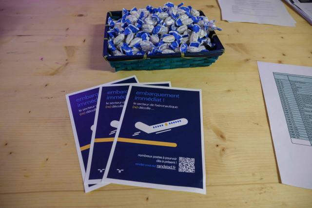 This photograph shows publicity materials displayed as job seekers and representatives of aerospace companies gather at an 'AeroDay' recruitment event organized by the Randstad Group, at the Stadium de Toulouse in Toulouse on January 22, 2026. According to organizers, some 2,800 positions are to be filled across the French aeronautics, defense and space industry sectors. (Photo by Ed JONES / AFP)