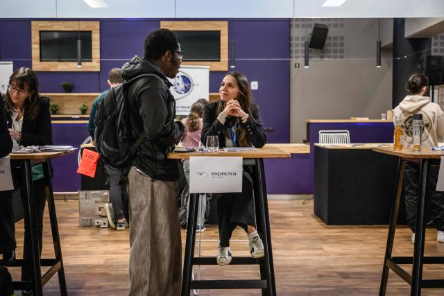 A Expectra representative speaks with an attendee at a table at an 'AeroDay' recruitment event organized by the Randstad Group, at the Stadium de Toulouse in Toulouse on January 22, 2026. According to organizers, some 2,800 positions are to be filled across the French aeronautics, defense and space industry sectors. (Photo by Ed JONES / AFP)