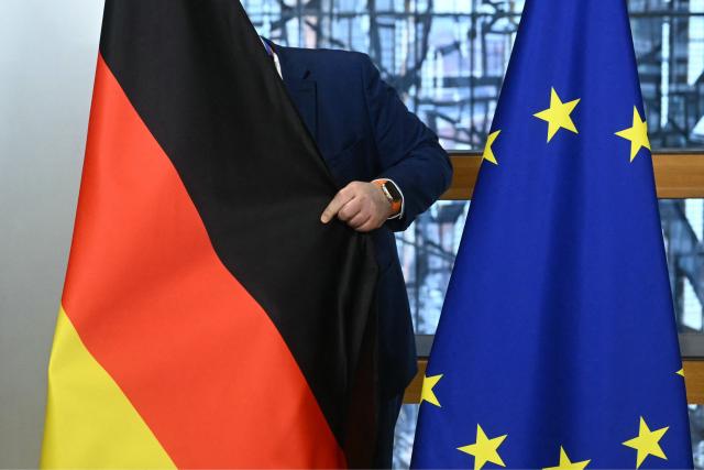 An employee sets up a German flag next to a EU flag ahead of a European Council meeting to discuss recent developments in transatlantic relations, in Brussels, on January 22, 2026. EU leaders meet on January 22, 2026, for an emergency summit on threats by US President to impose tariffs on countries opposed to his push to take Greenland, with crisis talks in Brussels coming to weigh potential countermeasures against the United States. (Photo by NICOLAS TUCAT / AFP)