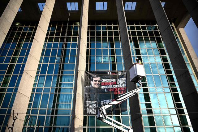 Workers install a banner demanding the release of jailed French journalist Christophe Gleizes on the facade of the Nouvelle Aquitaine region building in Bordeaux, south-western France on January 22, 2026. Gleizes was arrested in May 2024 while travelling to northeastern Algeria's Kabylia region to write about the country's most decorated football club, Jeunesse Sportive de Kabylie. (Photo by Christophe ARCHAMBAULT / AFP)