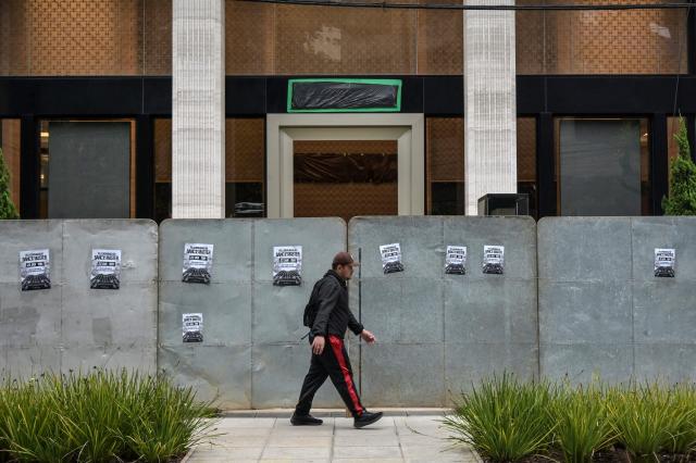 A passer-by walks past the Banco Master building protected by hoardings and with the bank's logo covered in plastic, in Sao Paulo, Brazil, on January 22, 2026, after Brazil's Central Bank ordered its shutdown due to a major liquidity crunch and "serious violations" of financial regulations. (Photo by NELSON ALMEIDA / AFP)