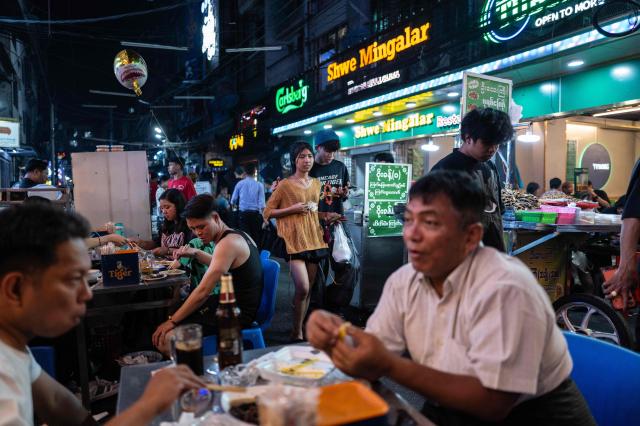 A couple walk past people eating in an outside restaurant in Chinatown, in Yangon, Myanmar, on January 22, 2026. (Photo by ANTHONY WALLACE / AFP)