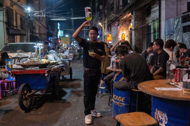 TOPSHOT - A waiter pours a drink for customers in an outside a bar in Chinatown in Yangon, Myanmar, on January 22, 2026. (Photo by ANTHONY WALLACE / AFP)