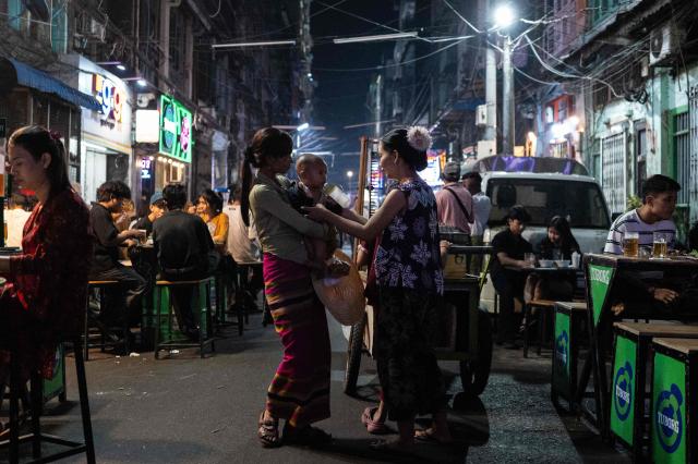 Two women talk while holding a baby in between bars and restaurants in Chinatown, in Yangon, Myanmar, on January 22, 2026. (Photo by ANTHONY WALLACE / AFP)