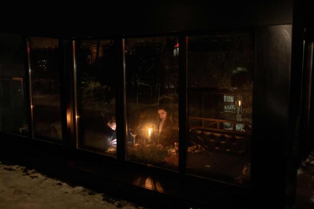 People sit in a dimly lit bar by candlelight during a power outage in Kyiv, on January 22, 2026, following Russian missile and drone attacks on Ukrainian energy infrastructure amid the Russian invasion in Ukraine. (Photo by Roman PILIPEY / AFP)