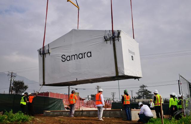 Workers prepare to secure the first free modular home for survivors of the 2025 Eaton Fire as it is lifted into place by a crane in Altadena, California, on January 22, 2025, more than a year after the fire destroyed some 9,400 structures. As part of its recovery efforts, the nonprofit coalition Steadfast LA has partnered with Samara, a modular house builder company, to provide homes at no cost to low-income Altadena and Pacific Palisades homeowners who lost their primary residences during the Eaton and Palisades wildfires of January 2025. (Photo by Frederic J. BROWN / AFP)