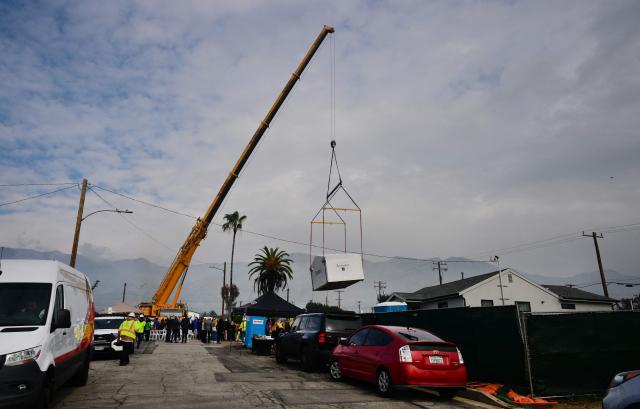 People gather to watch as the first free Modular Home for survivors of the 2025 Eaton Fire is lifted by a crane and put in place in Altadena, California on January 22, 2025, over a year after the fire destroyed some 9,400 structures. As part of its recovery efforts, the nonprofit coalition Steadfast LA has partnered with Samara, a modular house builder company, to provide homes at no cost to low-income Altadena and Pacific Palisades homeowners who lost their primary residences during the Eaton and Palisades wildfires of January 2025 (Photo by Frederic J. BROWN / AFP)