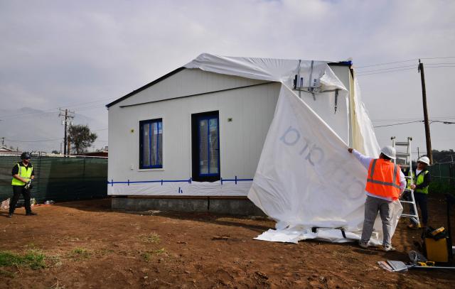 Workers remove the wrapping from the first free modular home for survivors of the 2025 Eaton Fire after it was set in place by a crane in Altadena, California, on January 22, 2025, more than a year after the fire destroyed some 9,400 structures. As part of its recovery efforts, the nonprofit coalition Steadfast LA has partnered with Samara, a modular house builder company, to provide homes at no cost to low-income Altadena and Pacific Palisades homeowners who lost their primary residences during the Eaton and Palisades wildfires of January 2025 (Photo by Frederic J. BROWN / AFP)