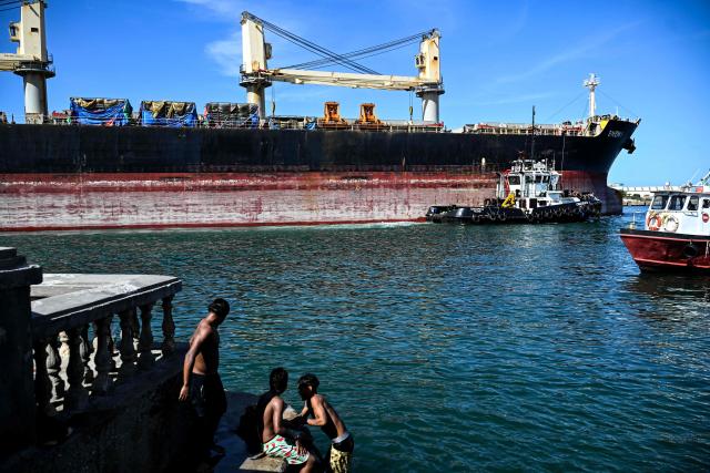 Children and a man bathe in front of the bulk carrier Shenli, sailing under the flag of Panama, in Puerto Cabello, Carabobo state, Venezuela, on January 22, 2026. (Photo by Ronaldo SCHEMIDT / AFP)