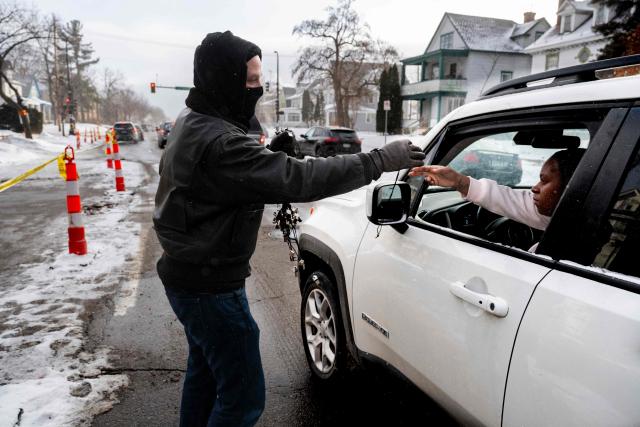 A man hands out whistles to people in cars passing by the memorial for Renee Nicole Good, in Minneapolis, Minnesota, on January 22, 2026. Residents of the city have taken to blowing whistles every time they spot ICE agents in the streets of the city. (Photo by ROBERTO SCHMIDT / AFP)
