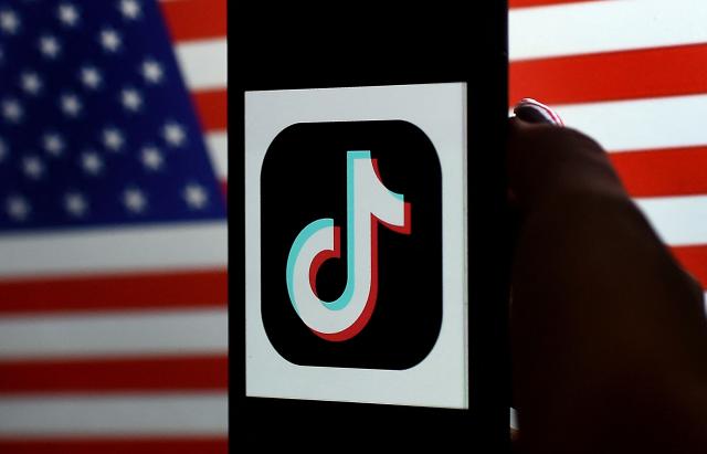 (FILES) In this photo illustration, the social media application logo, TikTok is displayed on the screen of an iPhone on a US flag background on August 3, 2020 in Arlington, Virginia. TikTok announced on January 22, 2026 that it has established a majority American-owned joint venture to operate its US business that will allow the company to avoid a ban over its Chinese ownership. The TikTok USDS Joint Venture LLC will serve more than 200 million users and 7.5 million businesses while implementing strict safeguards for data protection, algorithm security and content moderation, the company said. (Photo by Olivier DOULIERY / AFP)