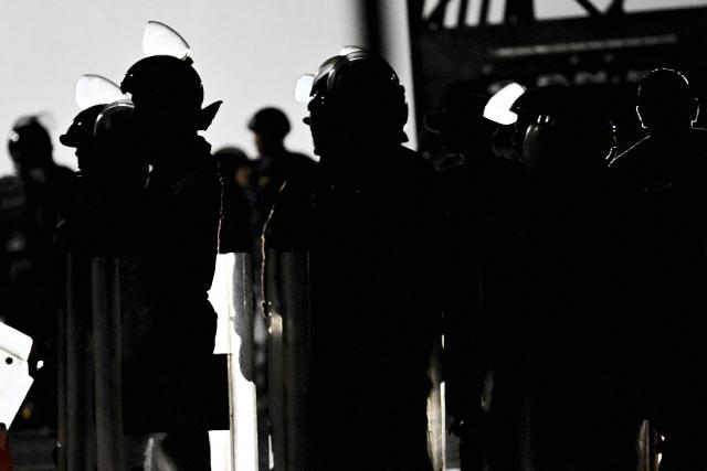 Riot police officers stand guard while relatives wait for news of prisoners in their tents set up outside Zone 7 of the Bolivarian National Police (PNB), also known as the Boleita Detention and Custody Center, in Sucre municipality, Caracas, on January 22, 2026. Exiled opposition figurehead Edmundo Gonzalez Urrutia on January 22 demanded "freedom for all people unfairly detained" in Venezuela, after the authorities released his son-in-law following a year in prison on terrorism charges. (Photo by Juan BARRETO / AFP)