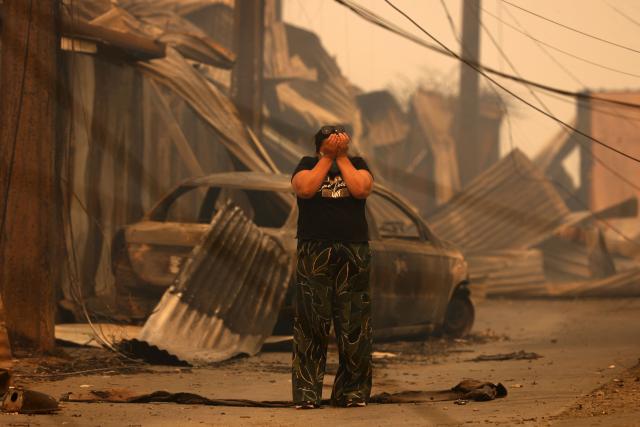 (FILES) A resident reacts in front of the charred remains of destroyed homes and a vehicle after a wildfire in Concepcion, Chile, on January 18, 2026. Chilean authorities announced on January 22, 2026, the arrest of a fourth person suspected of causing deadly wildfires that have ravaged the south of the country. The massive fires in recent days have killed at least 21 people and affected some 20,000 others. (Photo by Raul BRAVO / AFP)