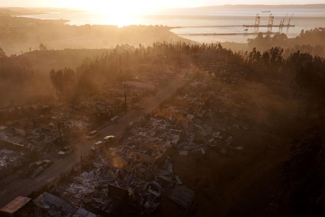 (FILES) Aerial view of the charred remains of destroyed homes at sunset after a wildfire in Concepcion, Chile, on January 18, 2026. Chilean authorities announced on January 22, 2026, the arrest of a fourth person suspected of causing deadly wildfires that have ravaged the south of the country. The massive fires in recent days have killed at least 21 people and affected some 20,000 others. (Photo by Raul BRAVO / AFP)