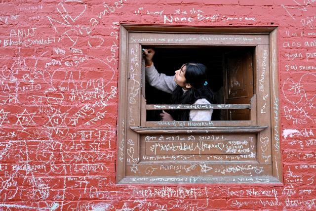 A woman writes a message with chalk on a wall at the Saraswati temple on the occasion of Hindu festival Basanta Panchami in Kathmandu on January 23, 2026. (Photo by PRAKASH MATHEMA / AFP)