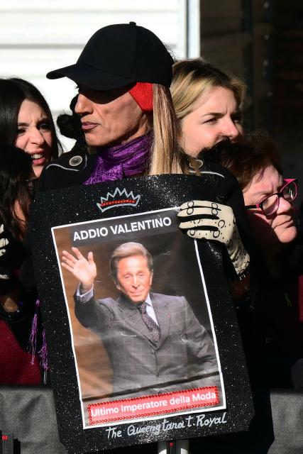 A man holds a placard with an image of the late Italian fashion designer Valentino Gavarani outside the Basilic of Santa Maria degli Angeli e dei Martiri during its funeral ceremony in Rome on January 23, 2026. (Photo by Stefano RELLANDINI / AFP)
