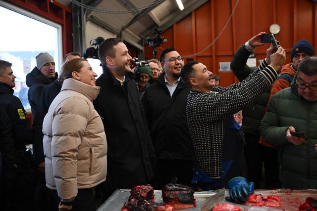 Danish Prime Minister Mette Frederiksen (3rd L) and Greenland's Prime Minister Jens-Frederik Nielsen (4th L) pose for a selfie with a fish market worker in Nuuk, Greenland, on January 23, 2026. Frederiksen will hold talks with her Greenlandic counterpart after a turbulent week that saw US President Donald Trump back down from his threats to seize the Arctic island and agree to talks. Frederiksen travelled to the Greenland capital Nuuk from Brussels, where she held talks earlier with NATO Secretary General Mark Rutte, who reached a purported deal with Trump on Greenland at the World Economic Forum in Davos. (Photo by Jonathan Nackstrand / AFP)
