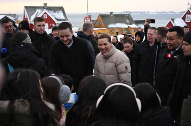 Danish Prime Minister Mette Frederiksen (C R) and Greenland's Prime Minister Jens-Frederik Nielsen (C L) react to locals and kids, in Nuuk, Greenland, on January 23, 2026. Frederiksen will hold talks with her Greenlandic counterpart after a turbulent week that saw US President Donald Trump back down from his threats to seize the Arctic island and agree to talks. Frederiksen travelled to the Greenland capital Nuuk from Brussels, where she held talks earlier with NATO Secretary General Mark Rutte, who reached a purported deal with Trump on Greenland at the World Economic Forum in Davos. (Photo by Jonathan Nackstrand / AFP)