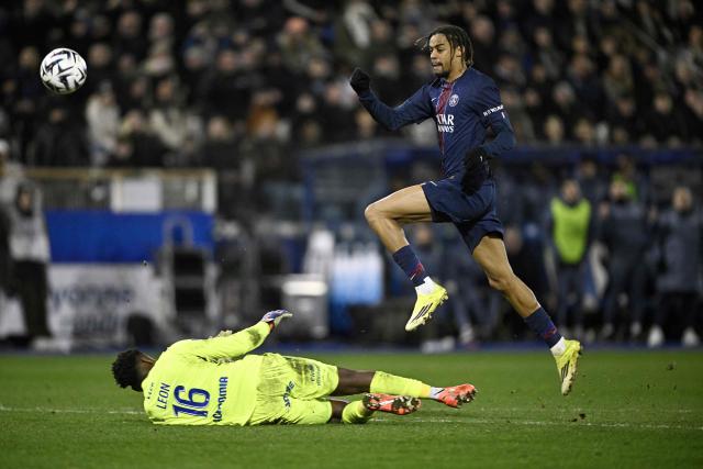 Paris Saint-Germain's French forward #29 Bradley Barcola jumps over Auxerre's French Guianese goalkeeper #16 Donovan Leon before scoring during the French L1 football match between  AJ Auxerre and Paris Saint-Germain (PSG) at Stade de l'Abbe-Deschamps in Auxerre on January 23, 2026. (Photo by JULIEN DE ROSA / AFP)