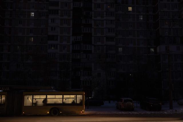 Passengers ride a bus past darkened apartment buildings on a freezing day during a power outage in a residential neighborhood of Kyiv on January 23, 2026, following Russian missile and drone attacks on Ukrainian energy infrastructure amid the Russian invasion in Ukraine. (Photo by Roman PILIPEY / AFP)